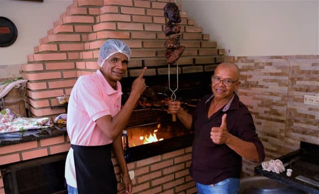 Tio Rosa de avental na churrasqueira ao lado de um cliente