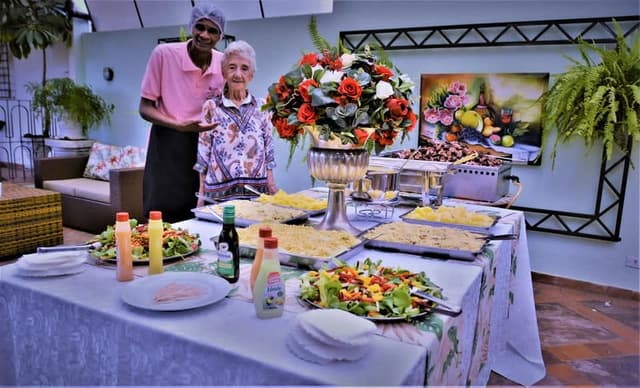 Buffet Tio Rosa ao lado de uma cliente idosa em frente a mesa de comidas